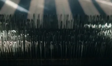 Rows of loom threads lit by shafts of light