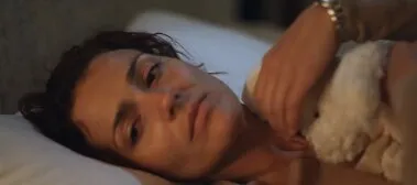 A grieving woman lies in bed clutching a soft toy